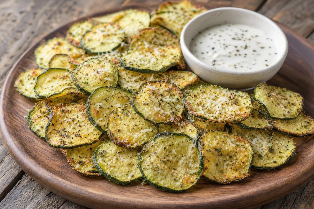 Golden crispy baked zucchini chips sprinkled with parmesan and Italian herbs on a wooden platter