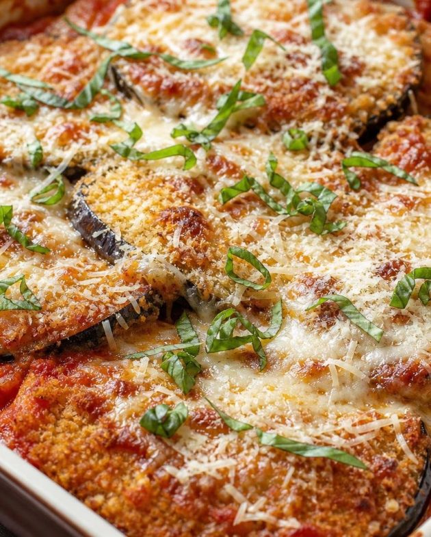 Baked Italian eggplant parmesan casserole with layers of breaded eggplant, tomato sauce, melted cheeses, and fresh basil garnish.