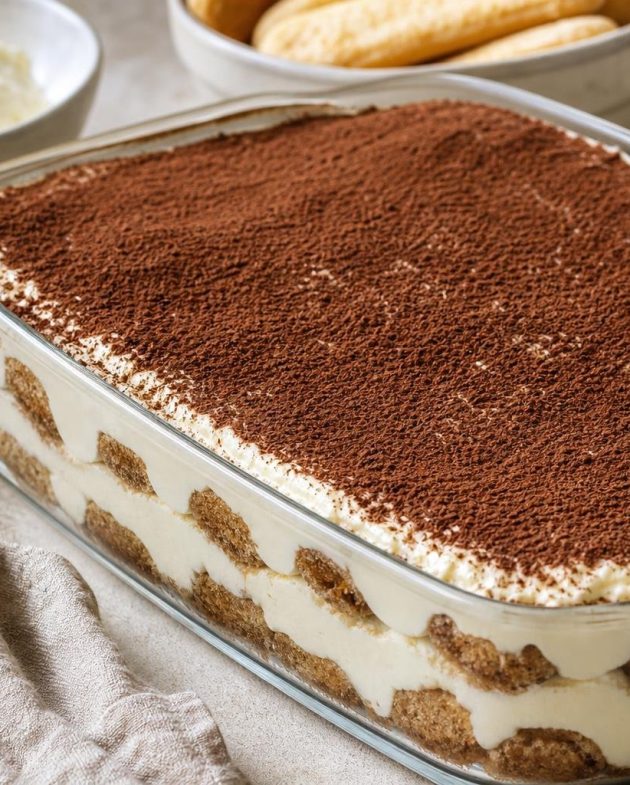 Classic Italian tiramisu dessert with layers of espresso-soaked ladyfingers and mascarpone cream dusted with cocoa powder in a glass dish.