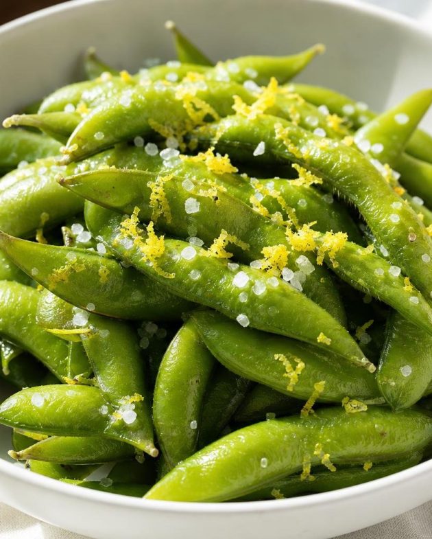 Steamed Japanese edamame pods sprinkled with sea salt and lemon zest in a white bowl