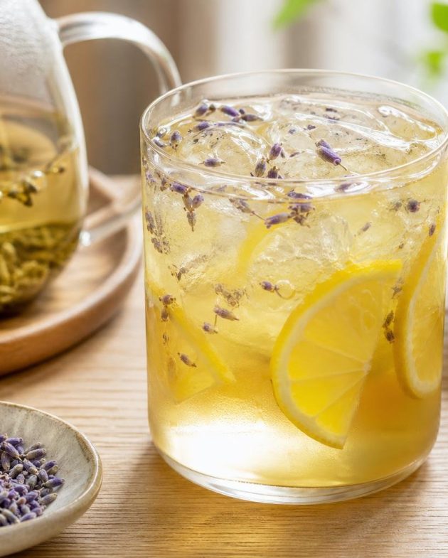 Glass of lavender and honey iced green tea garnished with lemon slices and ice cubes