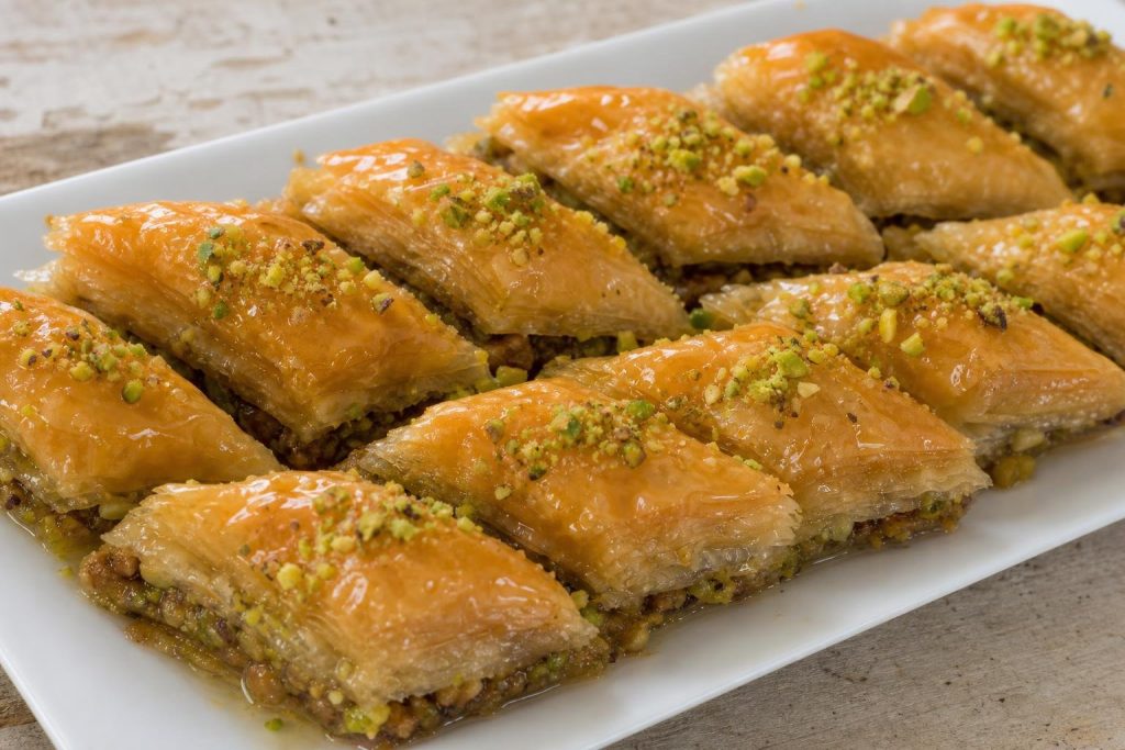 Slices of Middle Eastern baklava with honey and pistachio garnish on a white plate