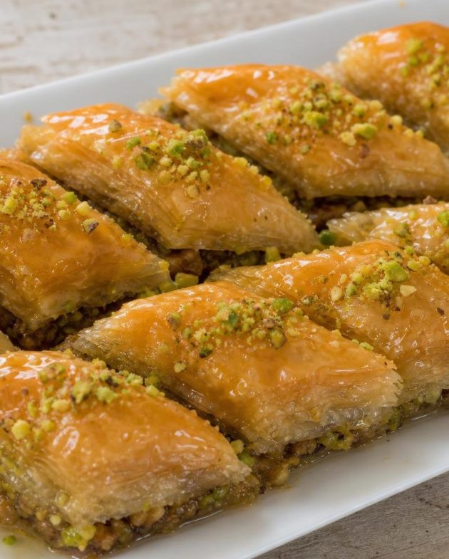 Slices of Middle Eastern baklava with honey and pistachio garnish on a white plate