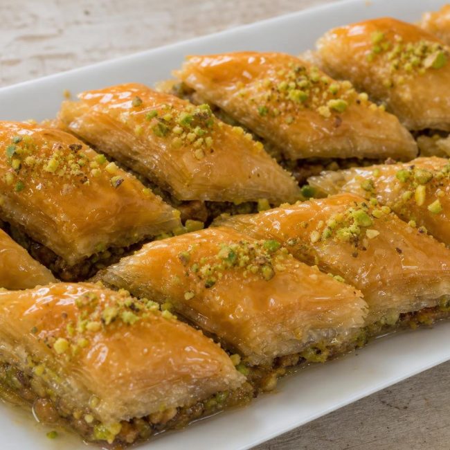 Slices of Middle Eastern baklava with honey and pistachio garnish on a white plate