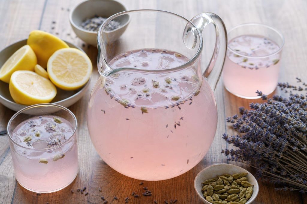 Glass pitcher of rose lemonade with cardamom and lavender, garnished with lemon slices and lavender sprigs