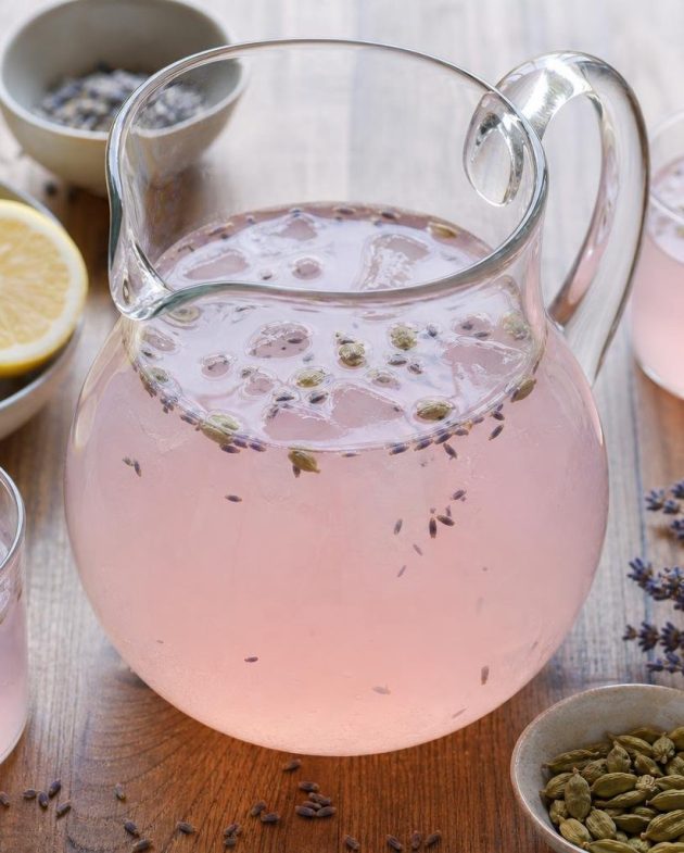 Glass pitcher of rose lemonade with cardamom and lavender, garnished with lemon slices and lavender sprigs