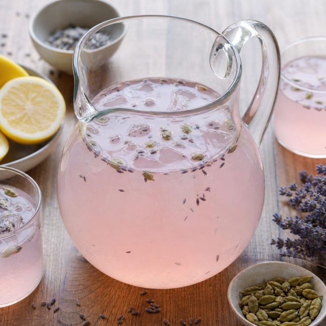 Glass pitcher of rose lemonade with cardamom and lavender, garnished with lemon slices and lavender sprigs