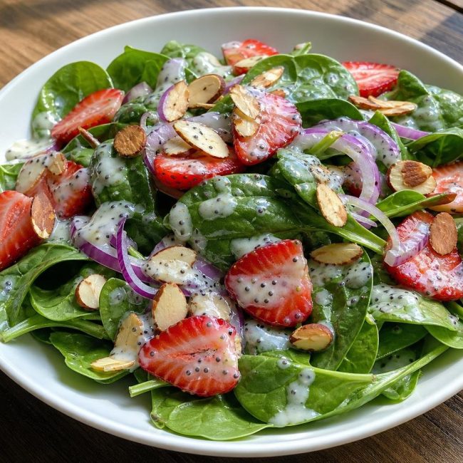 Bowl of spinach and strawberry salad with sliced almonds and poppy seed dressing
