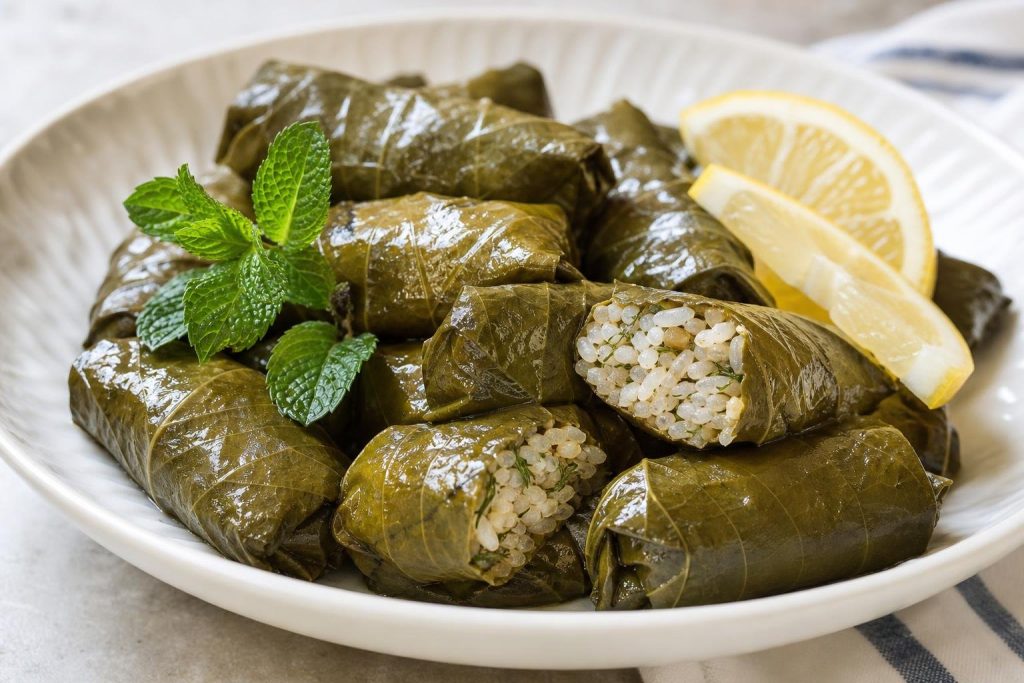 Plate of Greek dolmades stuffed grape leaves garnished with fresh mint and lemon wedges