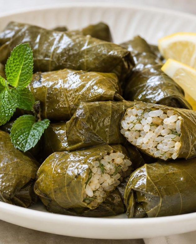 Plate of Greek dolmades stuffed grape leaves garnished with fresh mint and lemon wedges