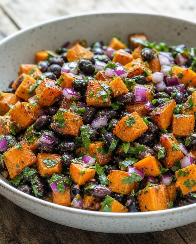 Sweet potato and black bean salad with cilantro-lime dressing served in a white bowl, garnished with cilantro leaves.