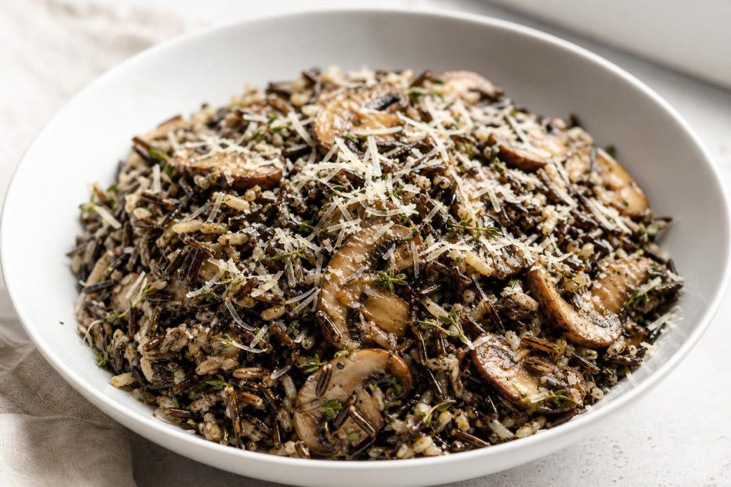 Warm wild rice salad with sautéed cremini mushrooms, fresh thyme, and grated parmesan cheese served in a white bowl.