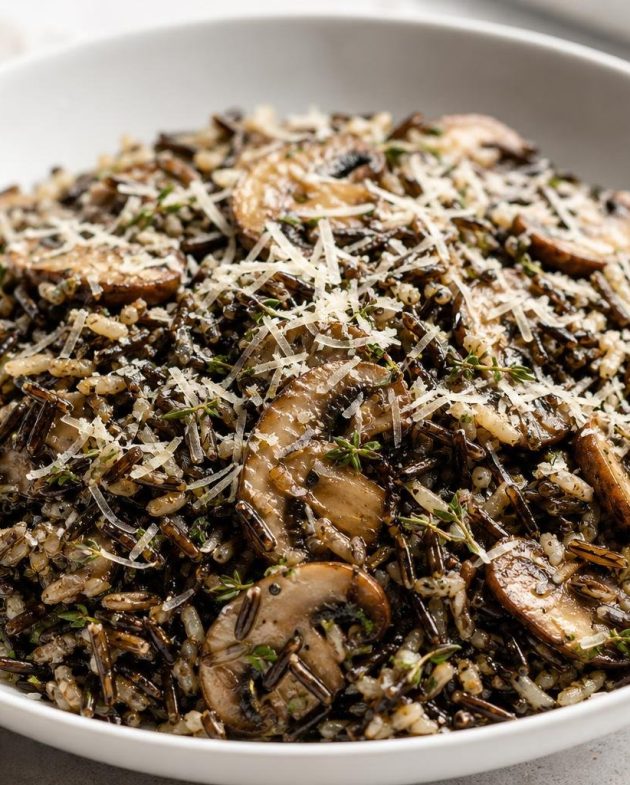 Warm wild rice salad with sautéed cremini mushrooms, fresh thyme, and grated parmesan cheese served in a white bowl.