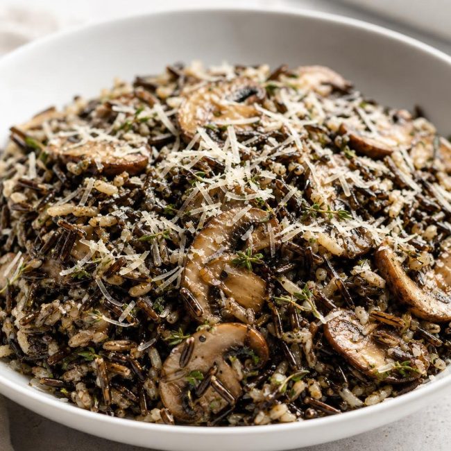 Warm wild rice salad with sautéed cremini mushrooms, fresh thyme, and grated parmesan cheese served in a white bowl.